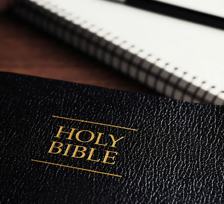 The Bible on a table next to a notebook.
